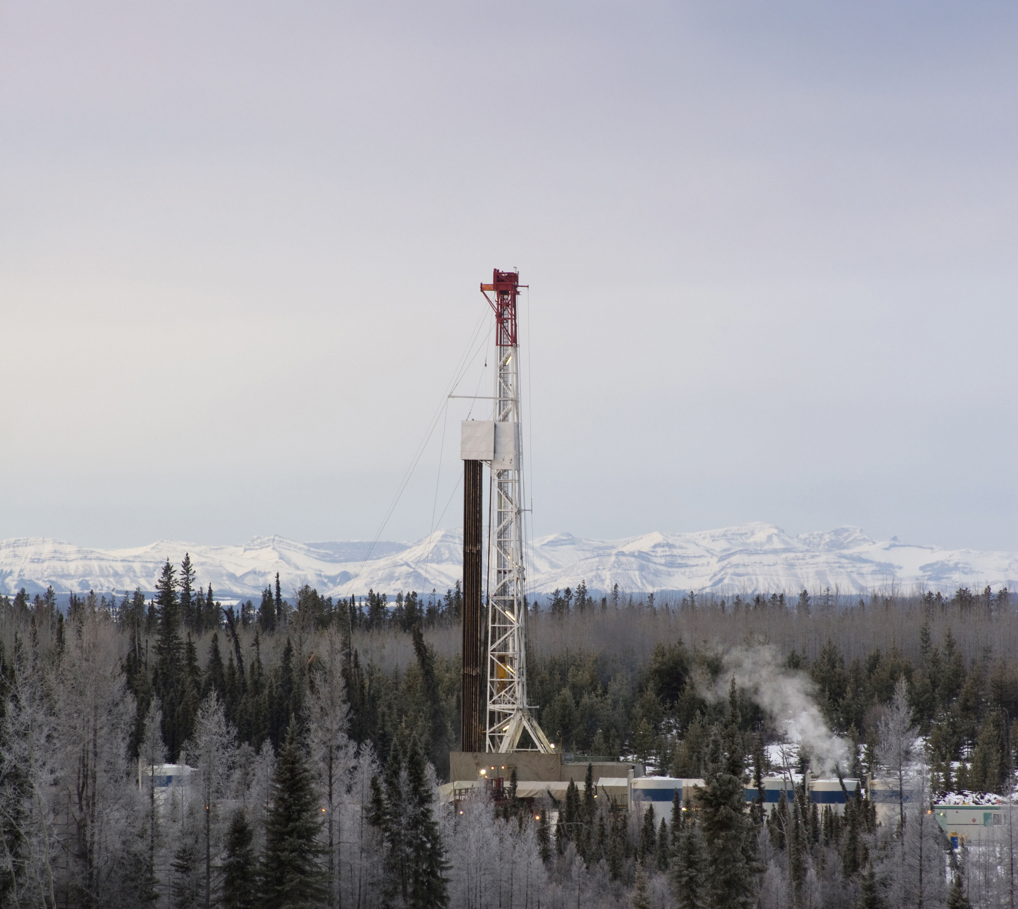 A oil drill rig in western Canada, the snowy rockies in the background