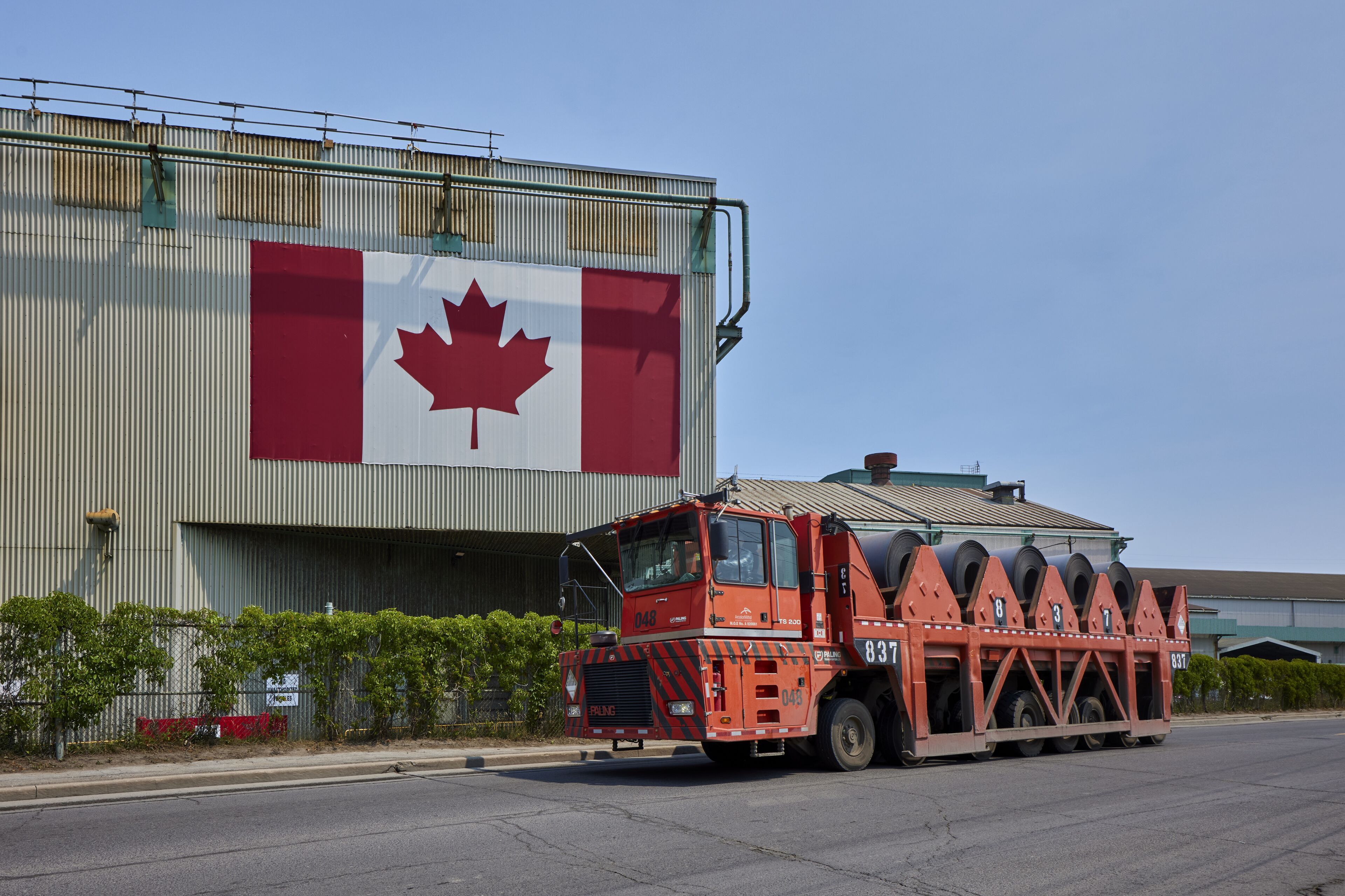 Coil hauler moves past building with Canadian flag